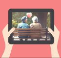 älteres Pärchen auf einer Parkbank von hinten mit Herzballon über ihnen, das Bild ist auf einem von zwei Händen gehaltenen Tablet zu sehen &copy; ebw mit Bild von Sarah/AdobeStock